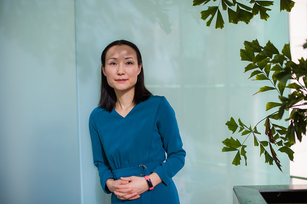 Female faculty member in blue dress leaning against a glass wall, MIT